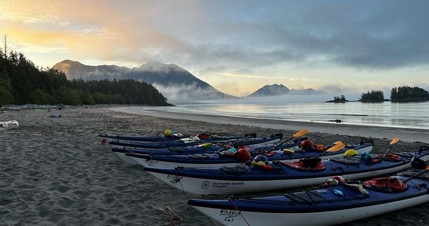 kayaks on a beach with ocean and mountains in the background