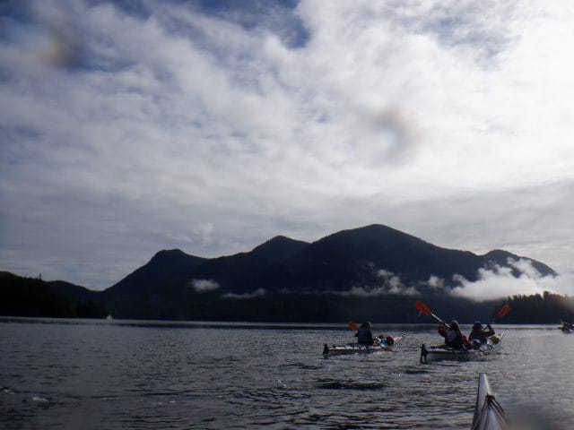 teens in kayaks on a lake with mountains behind them