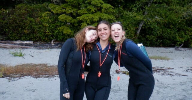 girls smiling in wet suits on a beach