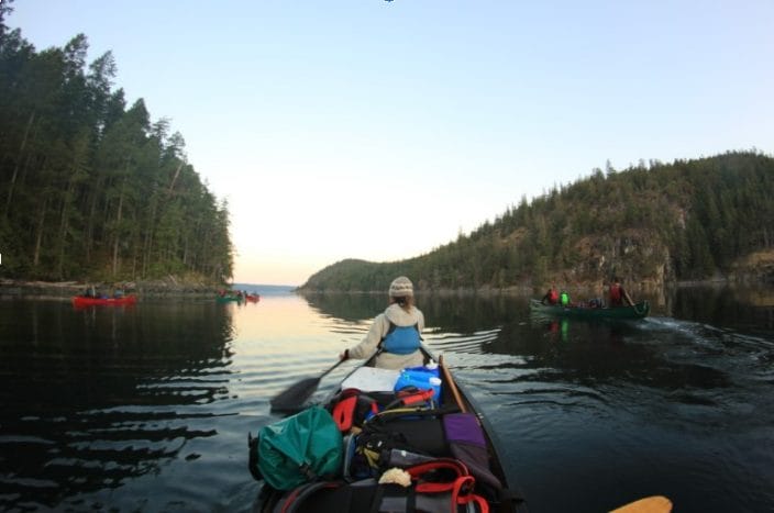 A woman paddles a canoe through calm waters in Desolation Sound, British Columbia