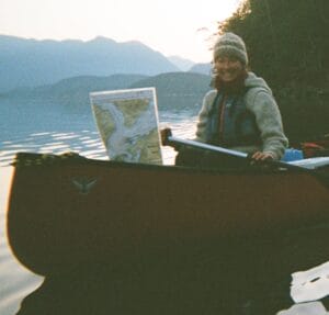 Young woman sits in a canoe on calm water and smiles at camera