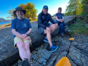 three men smiling sitting on a log