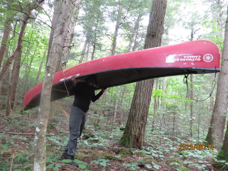 RIDHWANLAI BADMOS carries an Outward Bound Canada canoe on his back in a forest