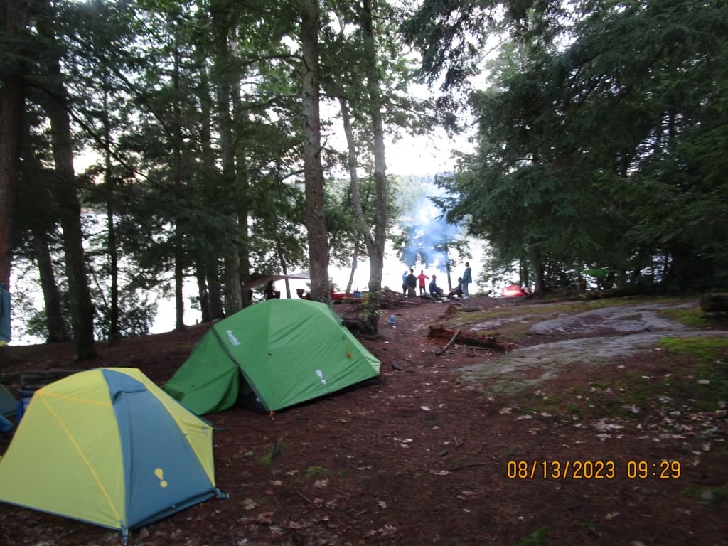 Two camping tents in a forest with a group playing on the back